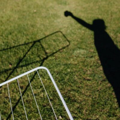 From above of metal dryer fragment with no clothes standing on grass outdoors and shadow of person imitating clothes hanging on drying rack on sunny summer day