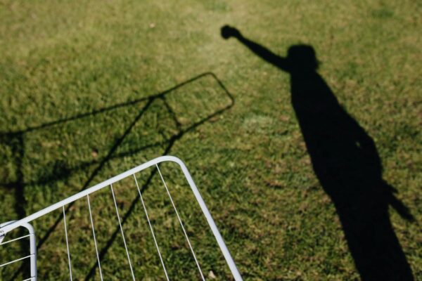 From above of metal dryer fragment with no clothes standing on grass outdoors and shadow of person imitating clothes hanging on drying rack on sunny summer day